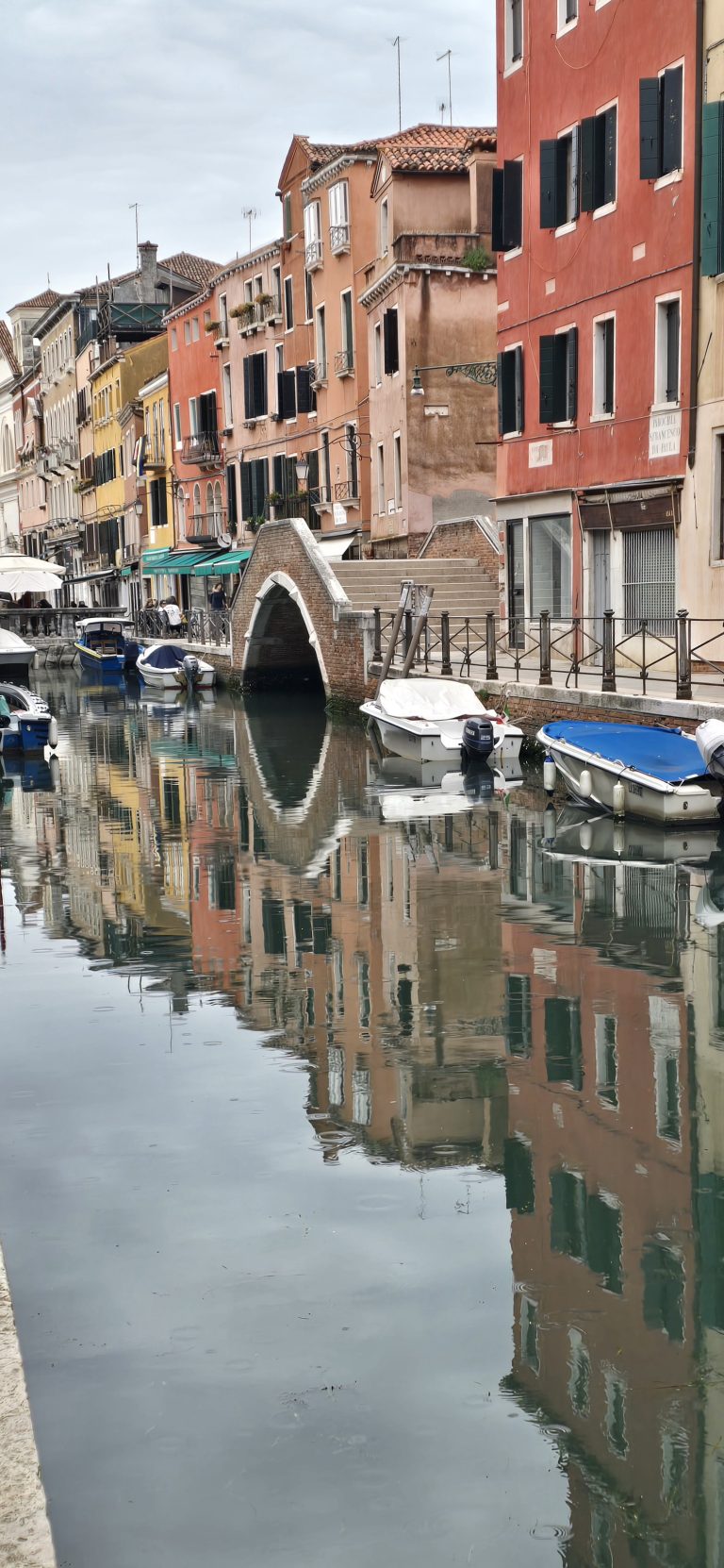 A Venice canal at rest, with a stone bridge and buildings mirrored in still water