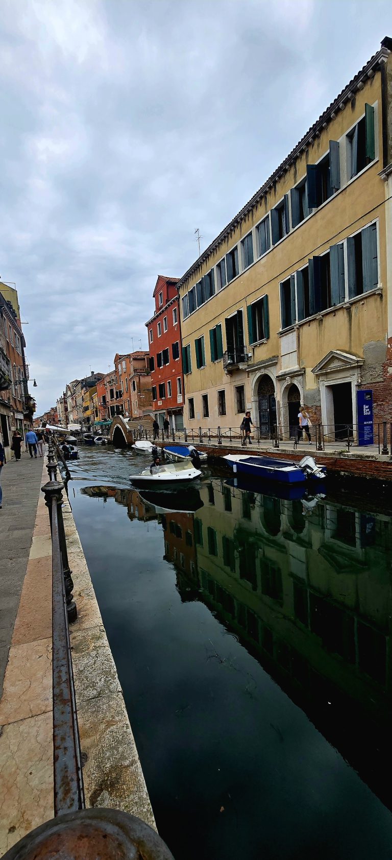 A quiet Venice canal lined with pastel buildings and moored boats under an overcast sky