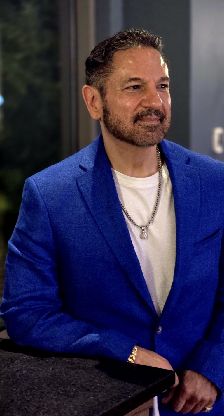 A man in a cobalt blue blazer leaning on a bar in a warmly lit restaurant