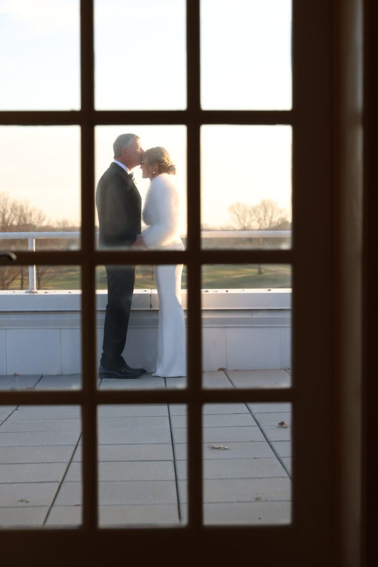 A couple silhouetted in an embrace, framed through a window pane at golden hour