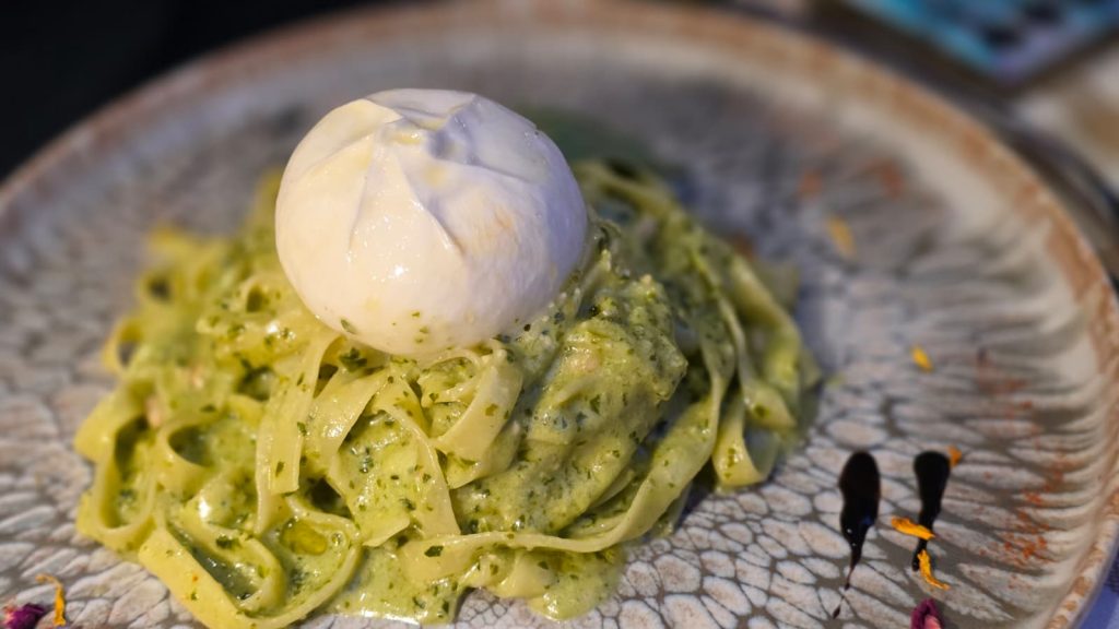 A ball of fresh burrata resting on a nest of bright green pesto pasta